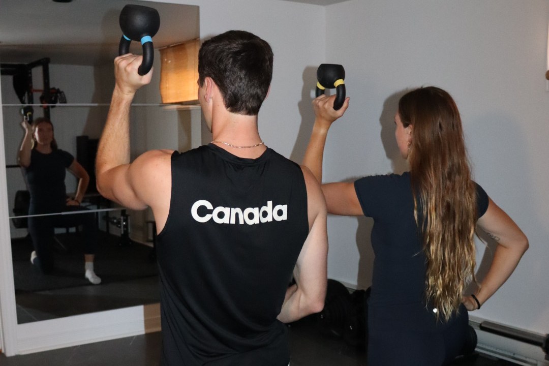 Maddie and a client in half-kneeling kettlebell presses, side by side in the studio gym.